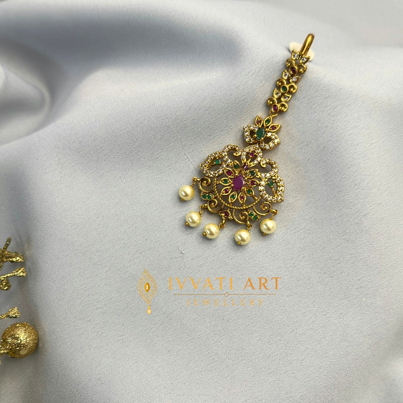 Antique gold floral maang tikka with ruby-emerald stones and pearl hangings – handcrafted by Ivvati Art Jewellery.