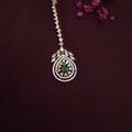 Green stone maangtikka with floral CZ design placed on bridal fabric