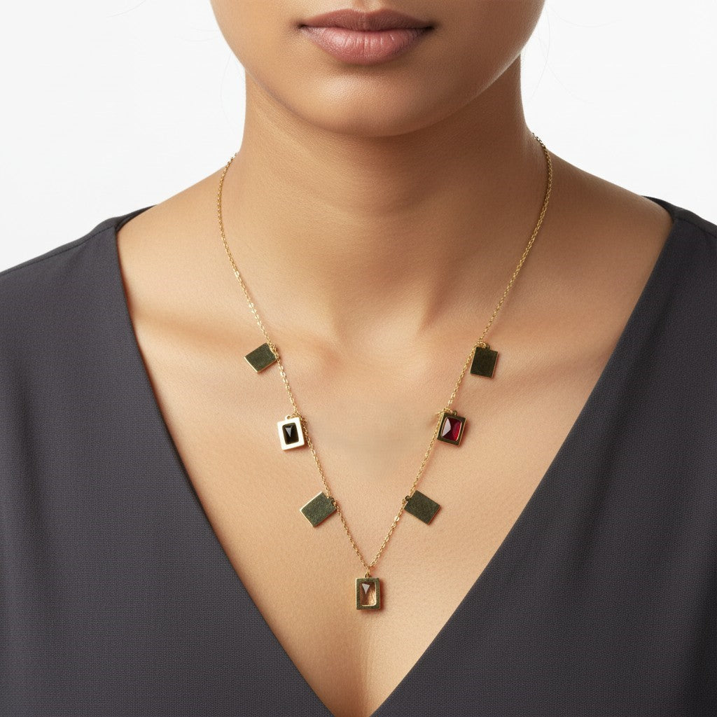 A gold-toned necklace with multiple small rectangular and square charms, worn by a model. Some charms are solid gold, while others feature dark green, black, and red inlay details.