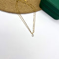Layered 18K gold plated chain with a solitaire CZ pendant placed on a white background beside a wooden prop

