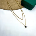 Two-layer gold chain necklace with a black stone pendant on a white fabric background

